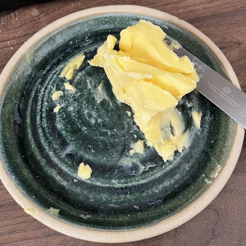 A green dish/plate with half a block of butter on it - the butter has been cut into numerous times.
