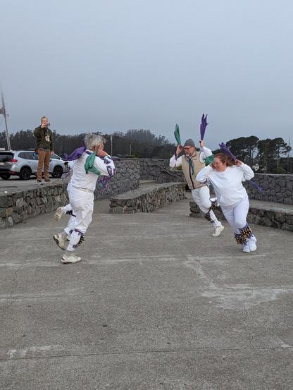 Four dancers in white costumes with bells and ribbons