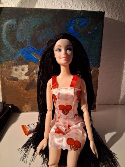 La muñeca sentada. Leva unos zapatos rojos de tacón cerrados y un vestido de tirantes rojo y blanco con dibujos de cerezas