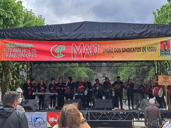 Grupo de Cavaquinhos num palco, com um banner da União dos Sindicatos de Viseu para o 1º de Maio, com o lema "Valorizar o trabalho e os trabalhadores"
