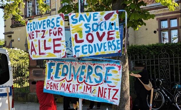 Drei bunte handgemalte Schilder an einem Metallgestänge
'Fediverse Netz für alle', 'Save Social Love Fediverse', 'Fediverse Deine Macht im Netz'