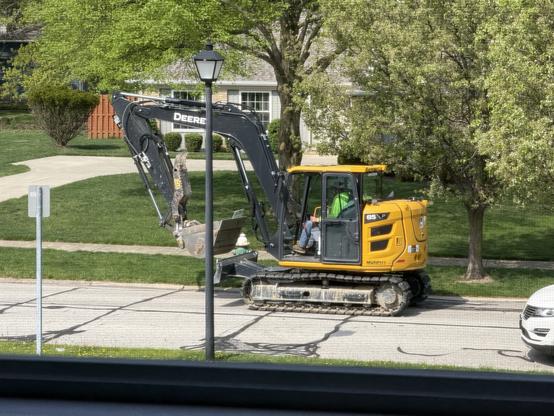 A yellow mini-excavator rolls down a suburban street.