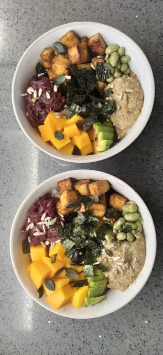 Two Buddha bowls with chopped mango, sweet pickled red cabbage, toasted tofu cubes, edamame beans, hummus, nori cuts and chopped avocado with sesame seeds sprinkled on top.