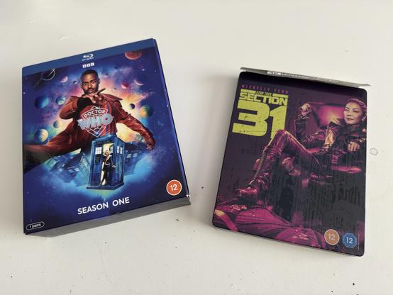 The image shows two Blu-ray box sets: "Doctor Who: Season One" featuring a character in a red coat and a blue police box against a cosmic background, and "Section 31" starring a character seated, with a dark and vibrant cover