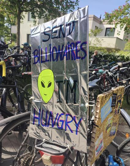 Demoschild mit dem Kopf eines Aliens und der Aufschrift "Send Billionaires, I'm hungry"