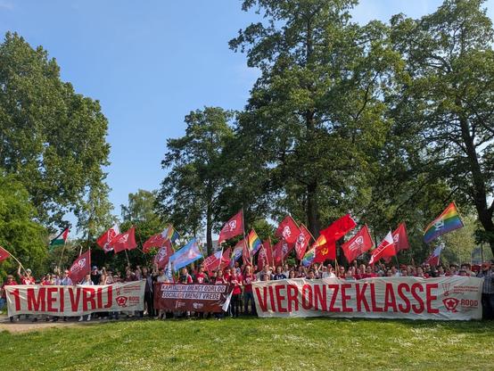 Groepsfoto van zo’n 100 mensen met veel vlaggen en spandoeken met teksten als “1 mei vrij” en “vier onze klasse”.