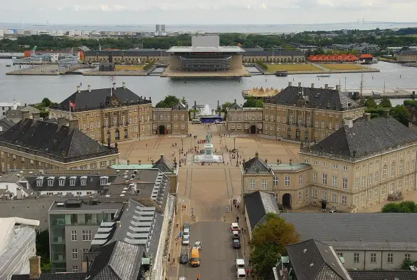 The image shows a large, open square surrounded by significant architectural structures, likely featuring historical buildings, with a view of a body of water in the background. There are various boats and modern structures visible, including what appears to be the Copenhagen Opera House. The scene seems to capture a blend of historical and contemporary architecture, typical of urban waterfront areas.

Image Credits: Wikimedia / Rob Deutscher from Melbourne, Australia / CC BY 2.0