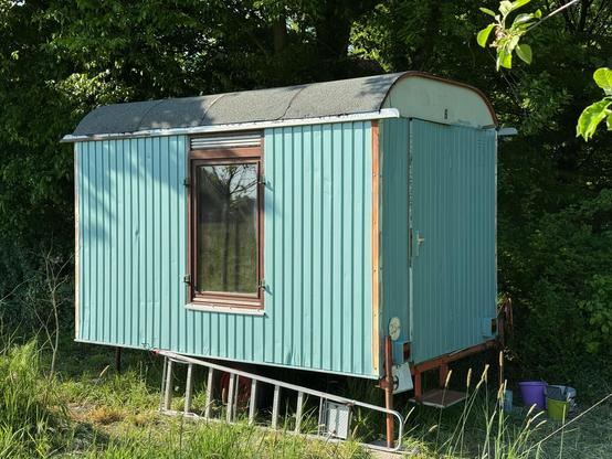 ein alter bauwagen, teilweise neu angestrichen in einen hellen grünblau ton