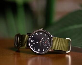 Una réplica del reloj de Joel, de The last of us, con la carátula intacta. Tiene extensible de tejido de nylon tipo militar, carátula en fondo negro con marcadores y números en color blanco, un pequeño cronómetro en el lugar de la hora sexta, cuya manecilla es color rojo.