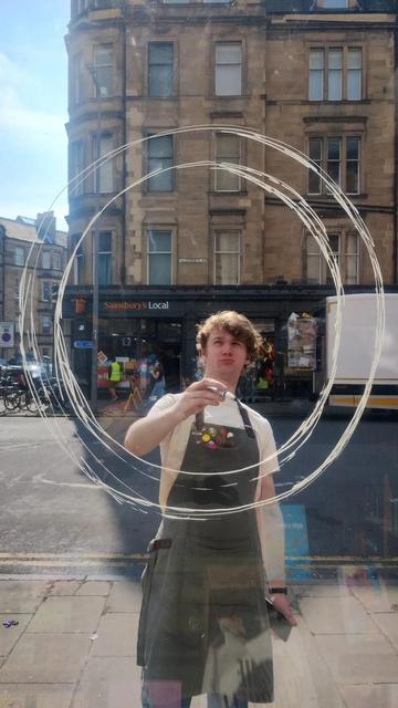 Looking out the front window of the Edinburgh Bookshop, as bookseller Jack starts painting a design on the glass