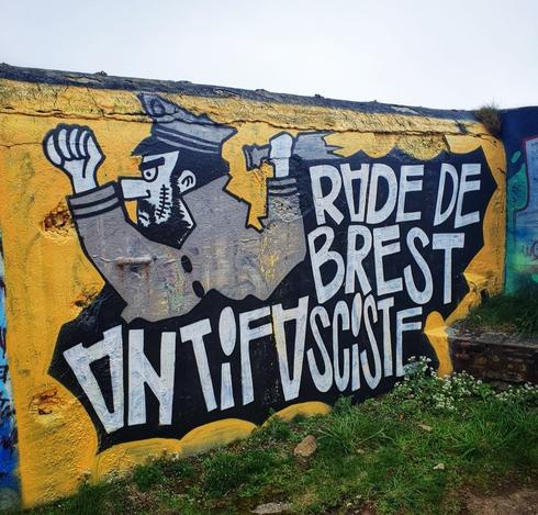 Fresque murale montrant une sorte de capitaine Haddock énervé et balafré, brandissant une bouteille en verre cassée sur fond jaune, avec l'inscription Rade de Brest antifasciste