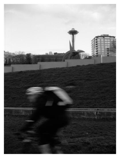 Foreground: blurry bike rider in the lower part of the frame; background: Space Needle in the upper part of the frame.