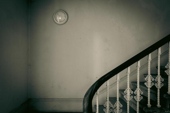 A blank wall, a light fixture and the curved banister of a stylish staircase.