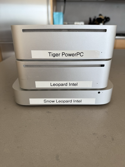 Three Mac Minis in a cute little stack. Label maker labels on them read “Tiger PowerPC”, “Leopard Intel”, and “Snow Leopard Intel”.