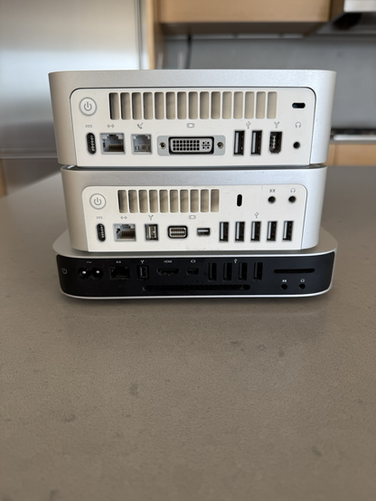 Three Mac Minis in a previous little stack, from behind. They indeed have different video-out ports.