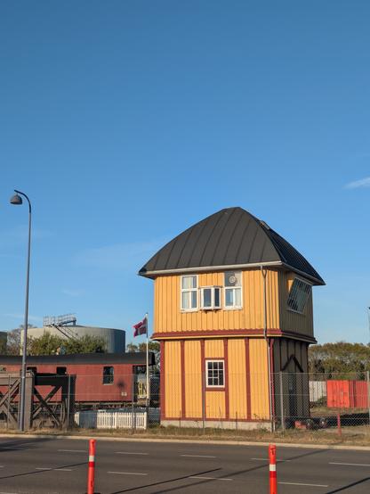 Foto des gelben Stellwerkturms im Fährhafen von Gedser, mit einem wehenden Dannebrog links daneben, überspannt von einem blauen Himmel.