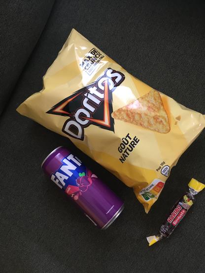 Sur le velour vert colvert d’un canapé, une canette de Fanta, un paquet de Doritos et un rouleau Haribo