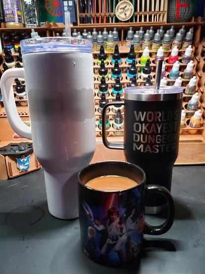 Photo of a regular coffee mug full of coffee flanked by two metal mugs... one of which is noticeably larger than the rest.