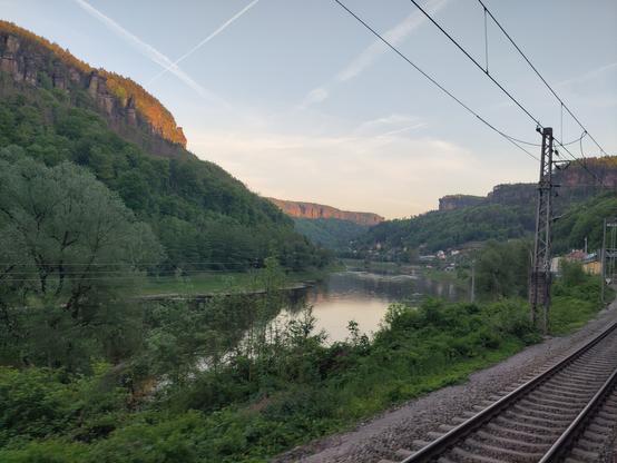 Elbe valley with luxurious green around. a rail track and at the back rocky mountains shining at sunset.