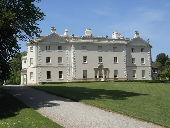 The image depicts a large, elegant mansion or house set in a landscaped garden. The building features a light-colored facade with multiple windows and a classic architectural style, including columns at the entrance. There is a gravel pathway leading up to the house, and the surrounding area appears to be well-maintained with grass and trees. The sky is clear, indicating a bright and sunny day.

Image Credits: Wikimedia / Lobsterthermidor 15:29, 27 May 2017 (UTC) / CC BY-SA 3.0