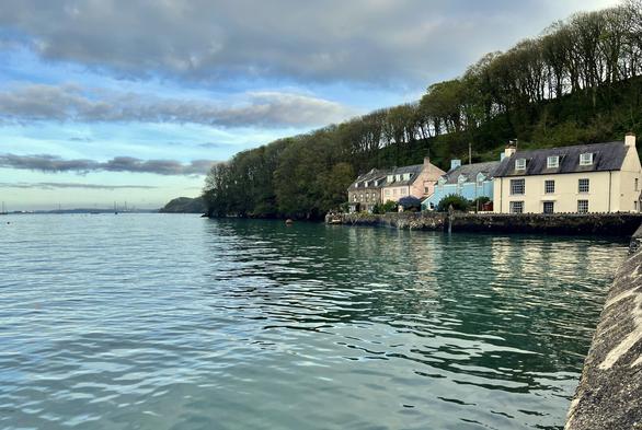 A colourful row of houses and the trees behind are reflected in the calm sea at high tide