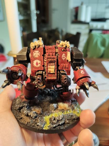 It's a Warhammer 40k Dreadnought, basically a gorilla shaped walking coffin with various dangerous weapons attached, photographed from the front. It's painted a dark red with black, and has skulls and candles on its shoulders.