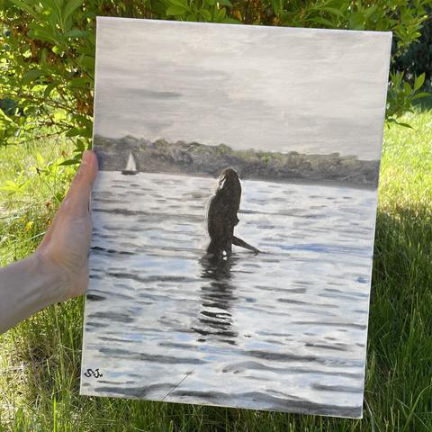 Eine Hand hält ein Gemälde, das eine Figur zeigt, die in ruhigem Wasser steht, umgeben von einer ruhigen Landschaft. Im Hintergrund ist ein Segelboot am Horizont zu sehen, wobei weiche Grautöne die Szene überwiegen.