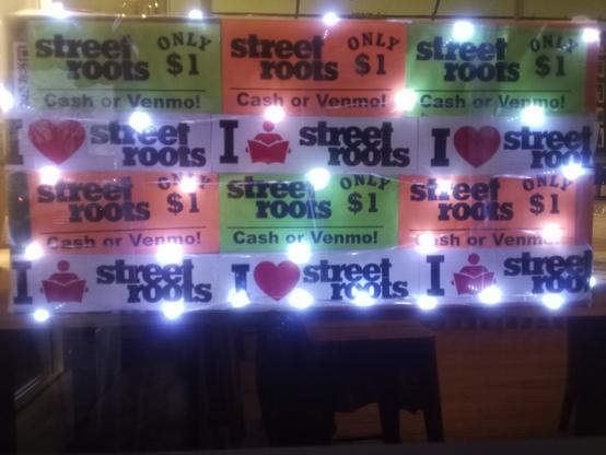 A poster with Street Roots stickers and lit up at 45th Parallel Wines in St John's  Portland Oregon