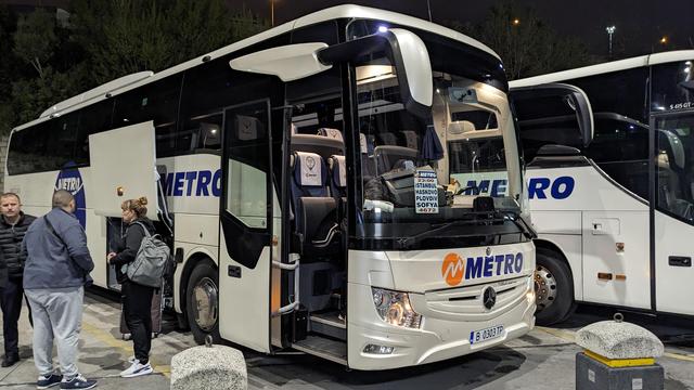 Outside of a modern travel bus. Some people are placing their luggage in the cargo bays.