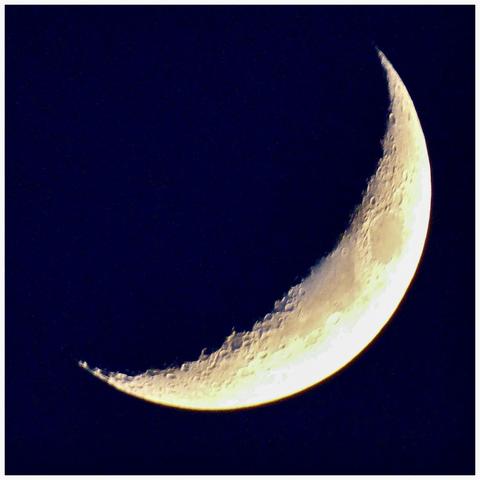 A close-up view of a crescent moon against a dark background, showcasing detailed craters and surface features.