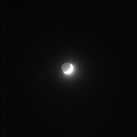 The image shows a crescent moon set against a dark night sky with scattered stars. The moon appears partially illuminated, with the bright portion creating a striking contrast against the surrounding darkness.