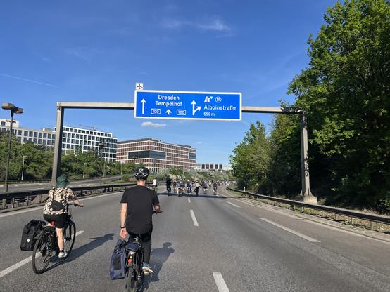 Teilnehmende einer Fahrraddemo auf der A100 westwärts, kurz vor Ausfahrt Alboinstraße. Ein Schild zeigt die Ausfahrt an. Es sind kleine Gruppen und viel Platz dazwischen.