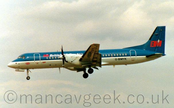 Side view of a blue and grey, twin propellor-engined airliner flying from right to left at a very low altitude, with undercarriage lowered and flaps extended from the rear of the wings, suggesting it is about to land.
The plane has dark blue upper surfaces and a grey belly, with white piping, and white "British Midland" titles on the upper forward fuselage next to a red "BM" logo.
This logo also appears in larger form on the tail.
The registration "G-BMYK" is on the lower rear fuselage in black.
Grey sky fills the rest of the frame.