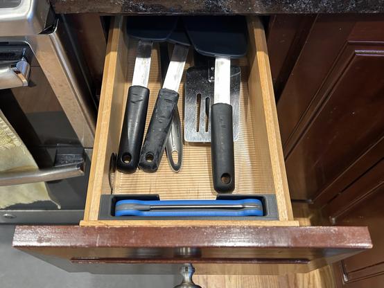 A narrow kitchen drawer is open.  It is full of silicone spatulas.  Across the front, there is a fitted black plastic insert with a Thermapen stored on edge.