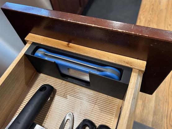 The kitchen drawer is open.  The Thermapen is in its black plastic insert.  There is a finger hole in the middle secton of the insert to lift the pen out.
