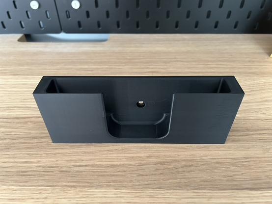 The 3D printed Thermapen insert is sitting alone on a shelf.  It is a black brick with a finger hole and a screw hole visible.