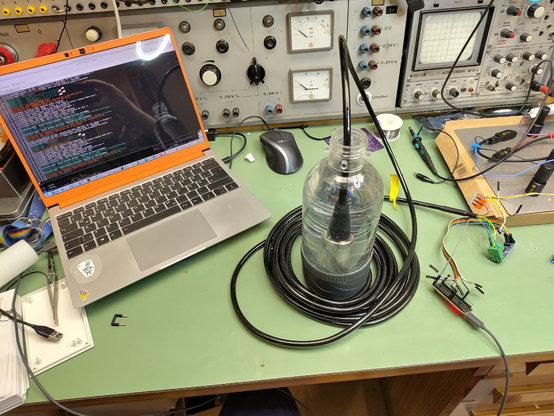 Ein Foto von meinem Basteltisch, links der Laptop, in der Mitte eine Sodamax-Plastikflasche mit einem großen zylindrischen Drucksensor darinnen. Daneben ein NodeMCU und ein RS-485-Modul die mit Jumper wires verbunden sind.