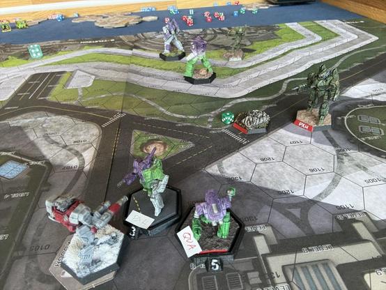 BattleTech game photo. Playing on an urban map, four Mechs in purple/white/green livery are surrounded by mechs in olive drab or grey and red. In the front, a Phoenix Hawk (represented by a Stinger) is directly in front of a Panther that it has just punched in the head. Twice.