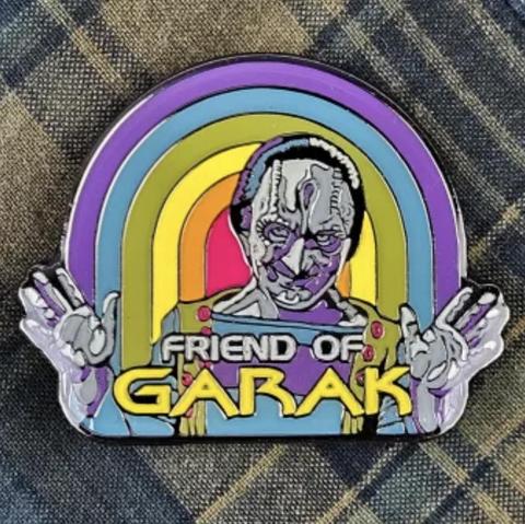 A colorful enamel pin featuring the Cardassian character Garak from Star Trek: Deep Space Nine, making a double peace sign with both hands. The background is a retro-style rainbow arch, and the text reads “Friend of Garak.”
