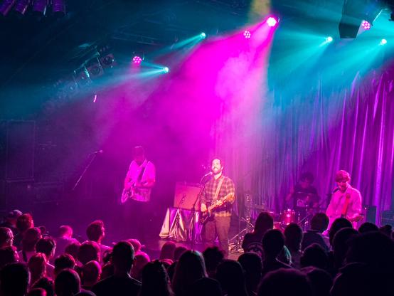 Herrenmagazin auf der Bühne getaucht in blaues, lilafarbenes Licht. Von Links König Wilhelmsburg Torben an der Gitarre, Deniz Jaspersen Gitarre und Gesang, Rasmus Engler Schlagzeug und Paul Konopacka Bass und Gesang.