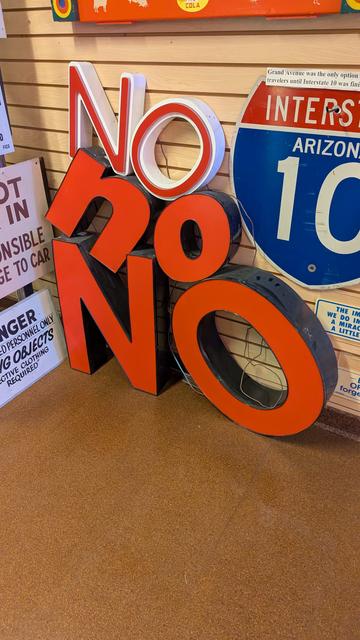 Big plastic sign letters that say "NO no NO" leaned against a wall, next to an interstate sign for I-10.