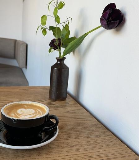 A dark tulip in a vase, near a coffee cup