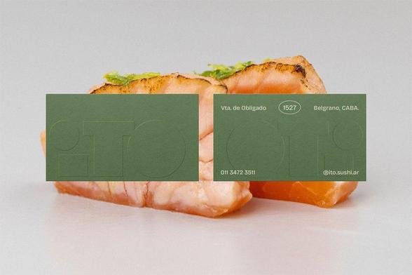 Two pieces of grilled salmon sushi topped with green garnish, partially covered by two green business cards displaying contact information.