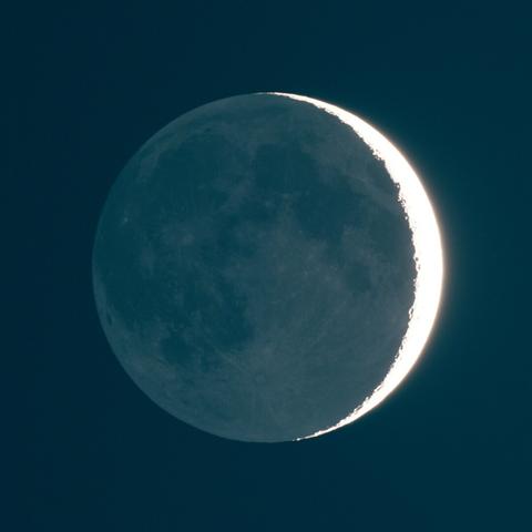 Photo of the moon, but the dark face is visible and lit crescent of the moon is just an oversaturated sliver of light
