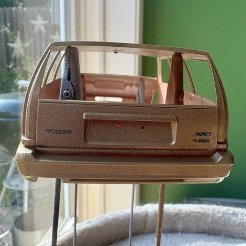 A close-up of the rear of the Champagne Metallic-painted plastic body of a Tamiya Volvo 850 Turbo station wagon model kit, showing the decal badges on the tailgate. To the left of the license plate recess is a "VOLVO" badge, while to the right an "850" badge sits above a "TURBO" badge.