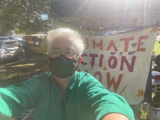 Masked woman in front of a homemade Climate Action Now sign