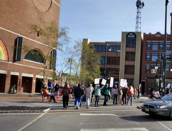 People gathering at a town square in front of an art museum, with a TV station building across the street.