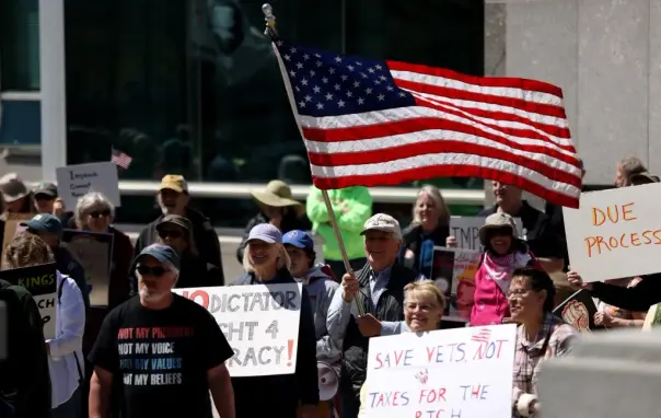 People holding signs in front of a building, one of them holds an American flag.
Some of the signs read: "No Dictator! Fight 4 Democracy!" and "DUE PROCESS"