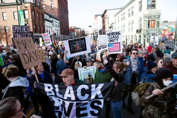People taking over a city street with signs. A white man in front has a banner that reads "Black Lives Matter".