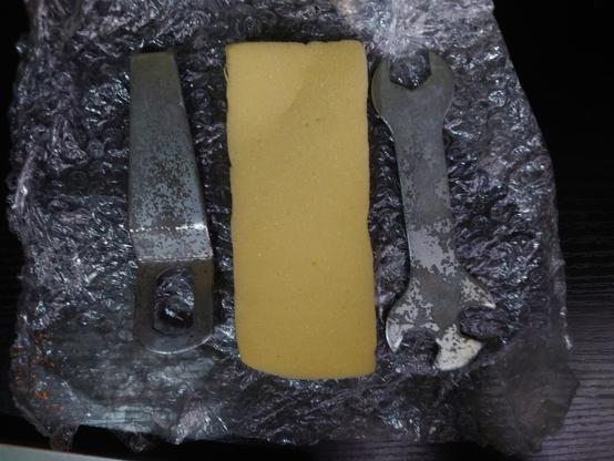 A spread of tools within the toolkit on some bubble wrap, showing from left to right, an angled flat cone spanner, a sponge, and a regular hex spanner, with one end with 2 different sizes used for various places on the C5.